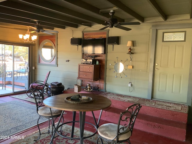 dining area featuring beam ceiling, ceiling fan with notable chandelier, and wood walls