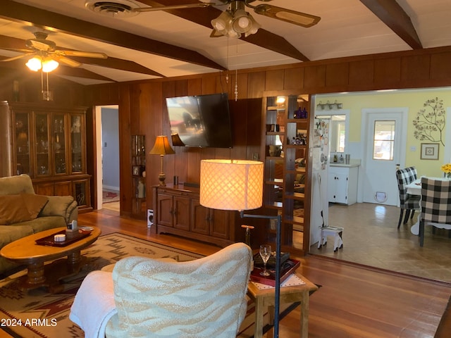 living room with hardwood / wood-style floors, beam ceiling, ceiling fan, and wood walls