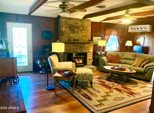 living room with wood walls, beamed ceiling, ceiling fan, a fireplace, and hardwood / wood-style floors