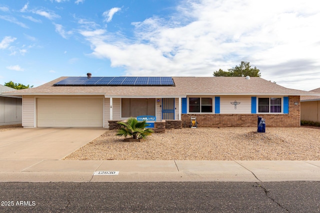 single story home with brick siding, solar panels, an attached garage, and concrete driveway