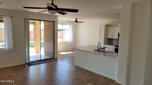 kitchen with tasteful backsplash, light stone counters, sink, ceiling fan, and white cabinets