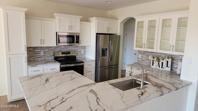 kitchen with light stone countertops, tasteful backsplash, stainless steel appliances, sink, and white cabinets