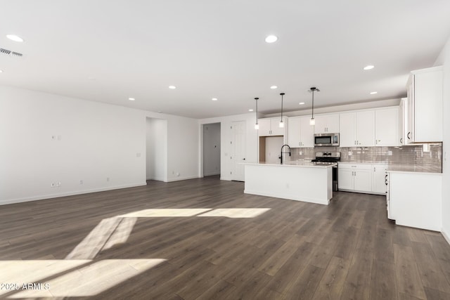 kitchen featuring appliances with stainless steel finishes, tasteful backsplash, a kitchen island with sink, white cabinets, and decorative light fixtures