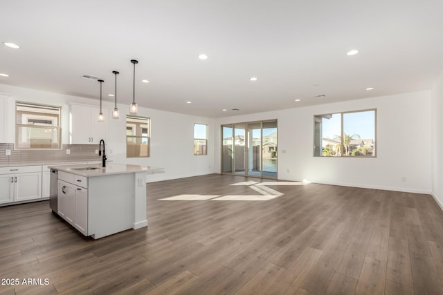 kitchen with wood-type flooring, stainless steel dishwasher, decorative light fixtures, white cabinetry, and an island with sink