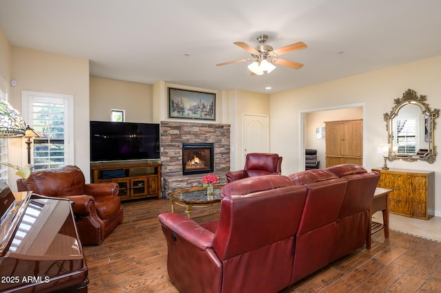 living room with plenty of natural light, ceiling fan, dark hardwood / wood-style flooring, and a stone fireplace