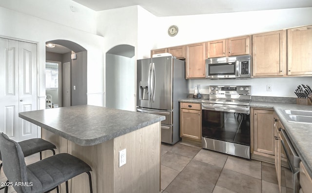 kitchen featuring stainless steel appliances, a breakfast bar area, arched walkways, dark countertops, and light tile patterned floors
