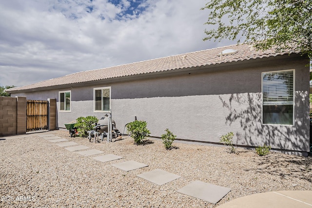 rear view of house with a gate, a tile roof, and stucco siding
