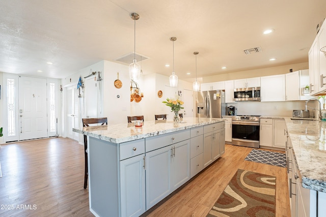 kitchen featuring pendant lighting, sink, stainless steel appliances, white cabinets, and a kitchen island