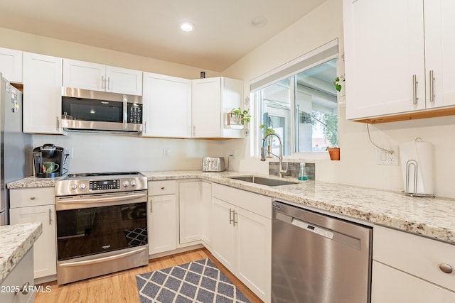 kitchen with appliances with stainless steel finishes, white cabinetry, sink, light stone counters, and light hardwood / wood-style flooring