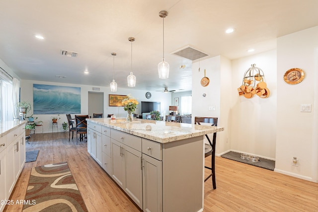 kitchen featuring a breakfast bar area, hanging light fixtures, light stone counters, light hardwood / wood-style floors, and a kitchen island