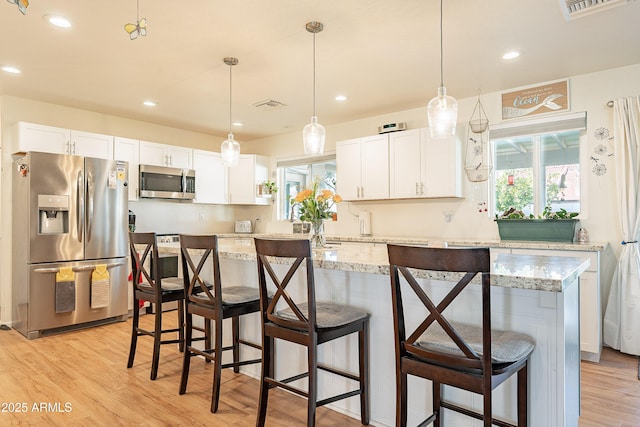 kitchen with white cabinetry, hanging light fixtures, stainless steel appliances, a kitchen breakfast bar, and a kitchen island