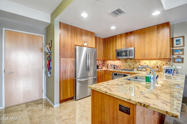 kitchen with sink, backsplash, kitchen peninsula, stainless steel appliances, and light stone countertops