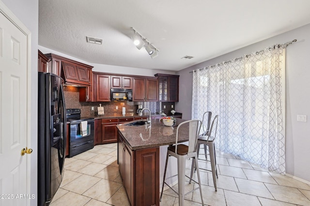 kitchen with tasteful backsplash, sink, a breakfast bar area, a kitchen island with sink, and black appliances