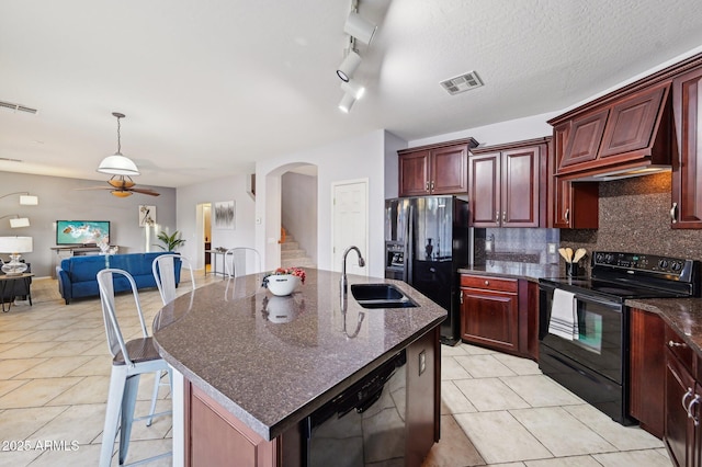 kitchen featuring sink, black appliances, hanging light fixtures, a center island with sink, and backsplash