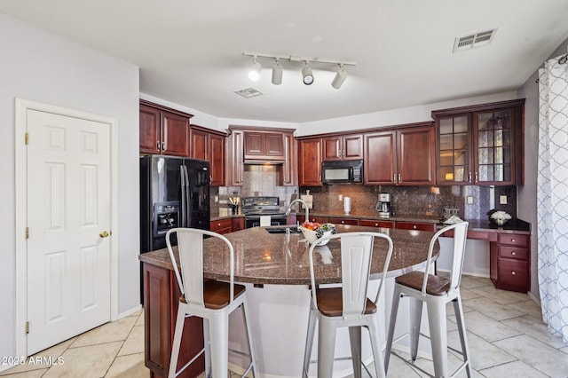 kitchen featuring a breakfast bar, a kitchen island with sink, tasteful backsplash, black appliances, and dark stone counters