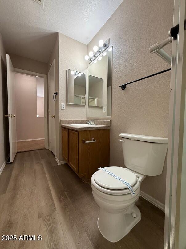 bathroom featuring wood-type flooring, toilet, a textured ceiling, and vanity