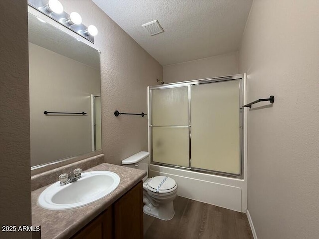 full bathroom with hardwood / wood-style flooring, combined bath / shower with glass door, vanity, a textured ceiling, and toilet