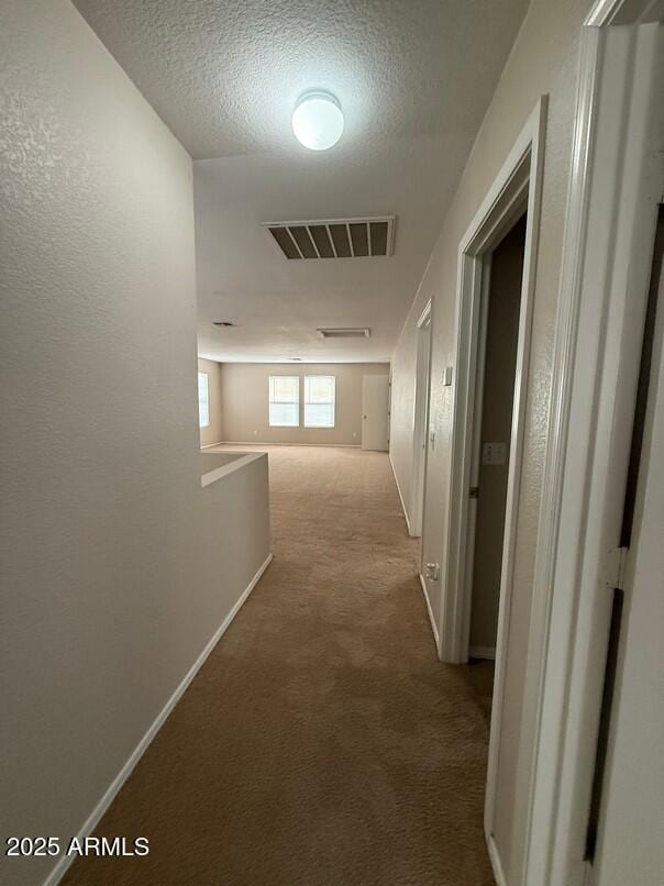 hall with light carpet and a textured ceiling