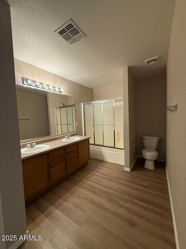 full bathroom with toilet, combined bath / shower with glass door, wood-type flooring, a textured ceiling, and vanity