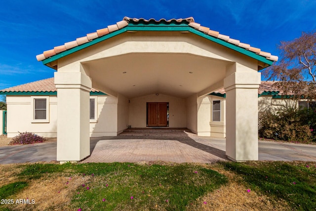 entrance to property with a tile roof, a patio, and stucco siding