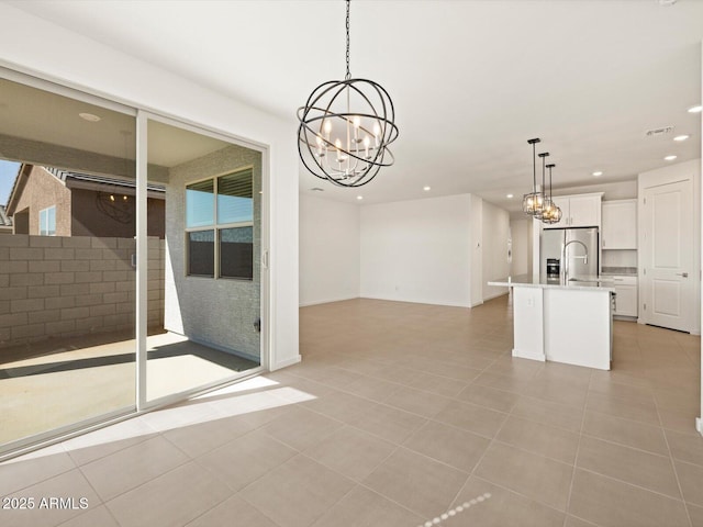 kitchen featuring open floor plan, a kitchen island with sink, stainless steel refrigerator with ice dispenser, white cabinetry, and pendant lighting