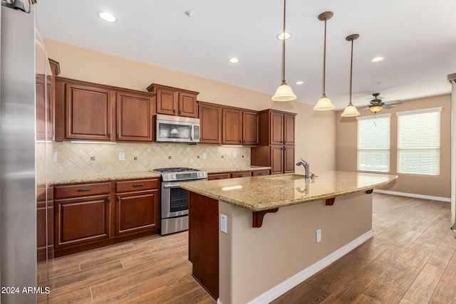 kitchen featuring an island with sink, a breakfast bar, light hardwood / wood-style floors, pendant lighting, and appliances with stainless steel finishes