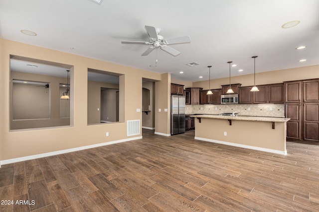 kitchen with stainless steel appliances, decorative backsplash, a breakfast bar area, and hardwood / wood-style flooring