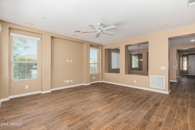 spare room with ceiling fan with notable chandelier, plenty of natural light, and dark wood-type flooring