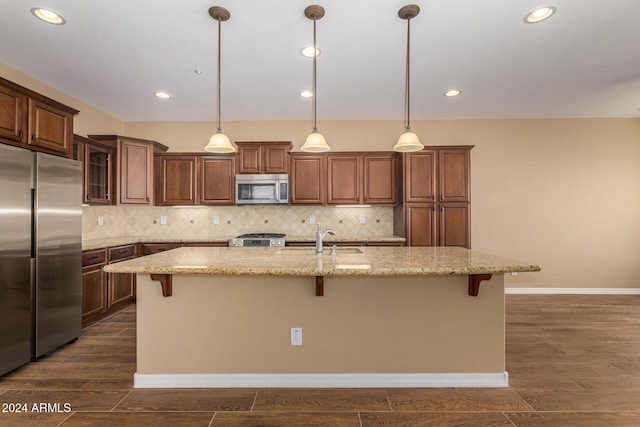 kitchen with stainless steel appliances, a breakfast bar area, a center island with sink, and dark hardwood / wood-style flooring