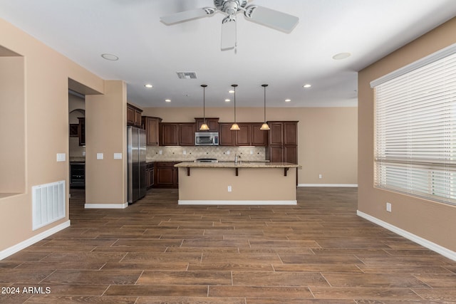 kitchen with pendant lighting, an island with sink, appliances with stainless steel finishes, a kitchen bar, and dark hardwood / wood-style flooring