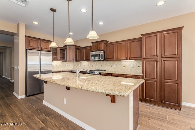 kitchen with hardwood / wood-style floors, appliances with stainless steel finishes, a breakfast bar, and a kitchen island with sink