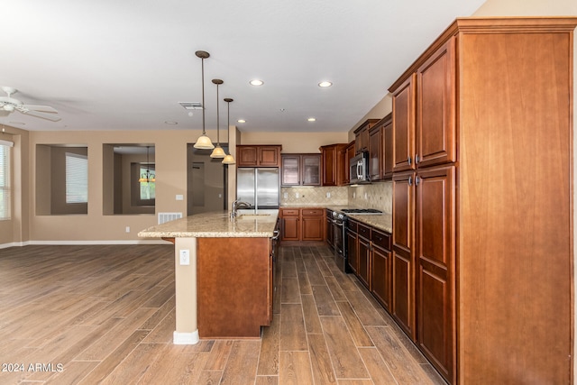 kitchen featuring a kitchen island with sink, wood-type flooring, stainless steel appliances, sink, and pendant lighting