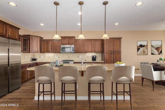 kitchen with tasteful backsplash, dark wood-type flooring, decorative light fixtures, stainless steel appliances, and an island with sink