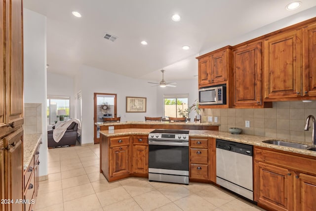 kitchen featuring lofted ceiling, sink, light stone counters, kitchen peninsula, and stainless steel appliances