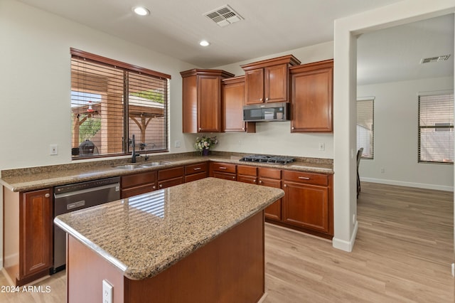 kitchen featuring sink, appliances with stainless steel finishes, a center island, light stone counters, and light wood-type flooring