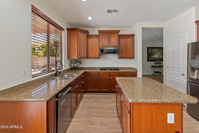 kitchen with sink, a center island, black appliances, light stone countertops, and light hardwood / wood-style flooring