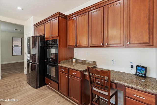 kitchen with dark stone countertops, built in desk, light hardwood / wood-style floors, and black appliances