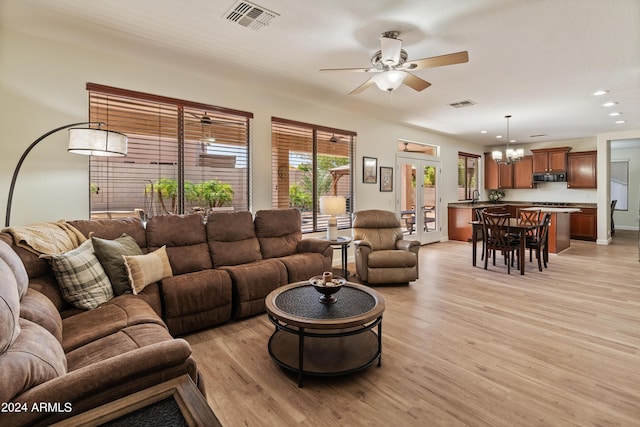 living room with ceiling fan with notable chandelier, french doors, and light wood-type flooring