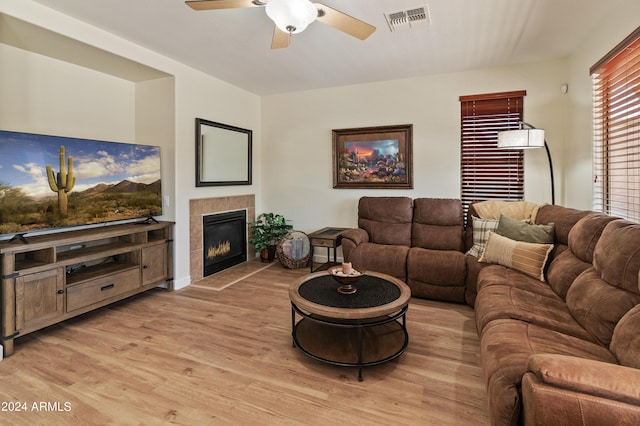 living room featuring a tiled fireplace, ceiling fan, and light wood-type flooring