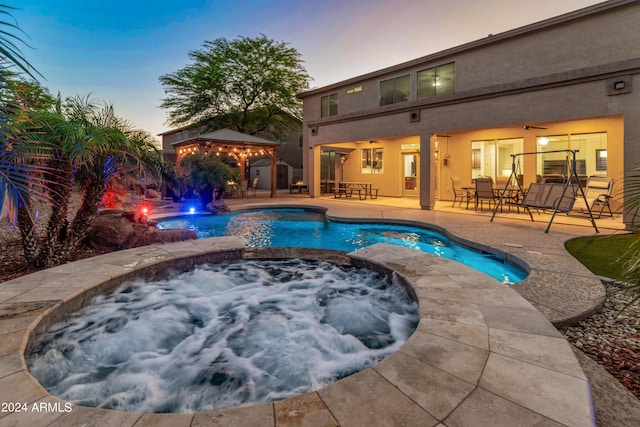 pool at dusk with an in ground hot tub, ceiling fan, and a patio