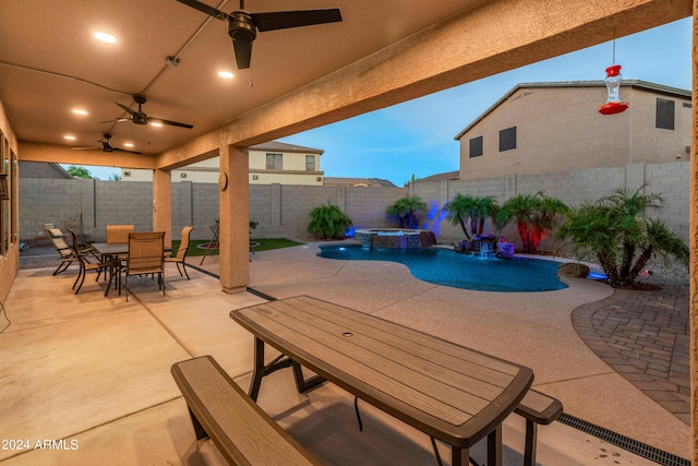 pool at dusk featuring pool water feature, ceiling fan, and a patio