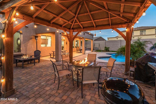 patio terrace at dusk featuring a fenced in pool, a fire pit, grilling area, and a gazebo