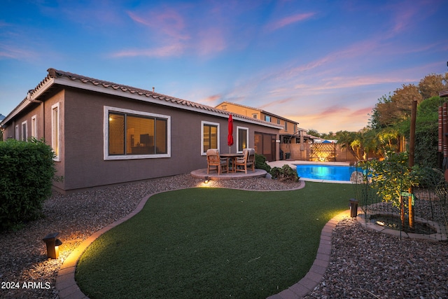 back house at dusk with a fenced in pool, a patio area, and a yard