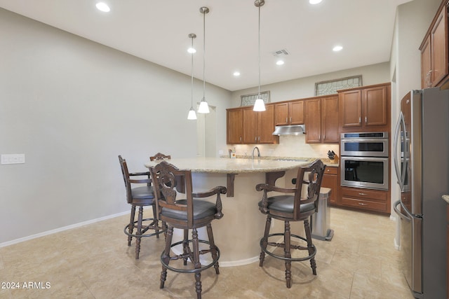 kitchen featuring appliances with stainless steel finishes, hanging light fixtures, an island with sink, a breakfast bar area, and light stone countertops