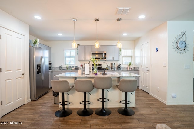 16425 W Latham St, Goodyear, AZ 85338 - kitchen featuring appliances with stainless steel finishes, a center island, wood finished floors, a breakfast bar, and recessed lighting