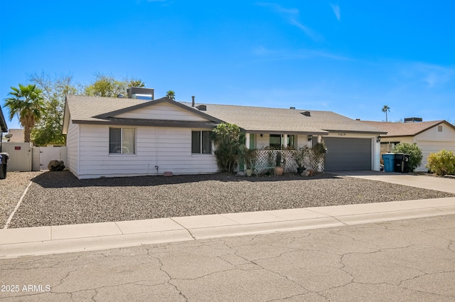 ranch-style home with driveway, a shingled roof, an attached garage, and fence