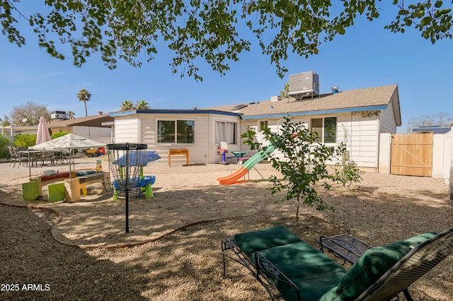 rear view of property featuring a playground, fence, central AC unit, a patio, and a gate