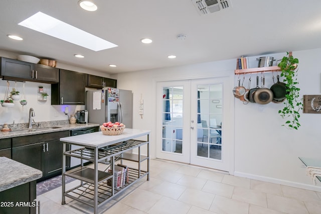 kitchen featuring visible vents, stainless steel refrigerator with ice dispenser, a sink, light stone counters, and a skylight