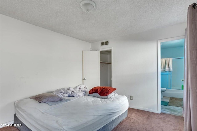 bedroom featuring a textured ceiling, ensuite bathroom, and light colored carpet