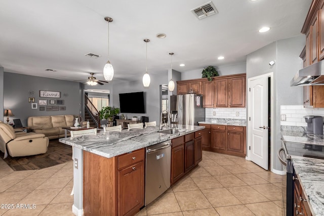 kitchen featuring pendant lighting, light tile patterned floors, a kitchen island with sink, stainless steel appliances, and light stone countertops